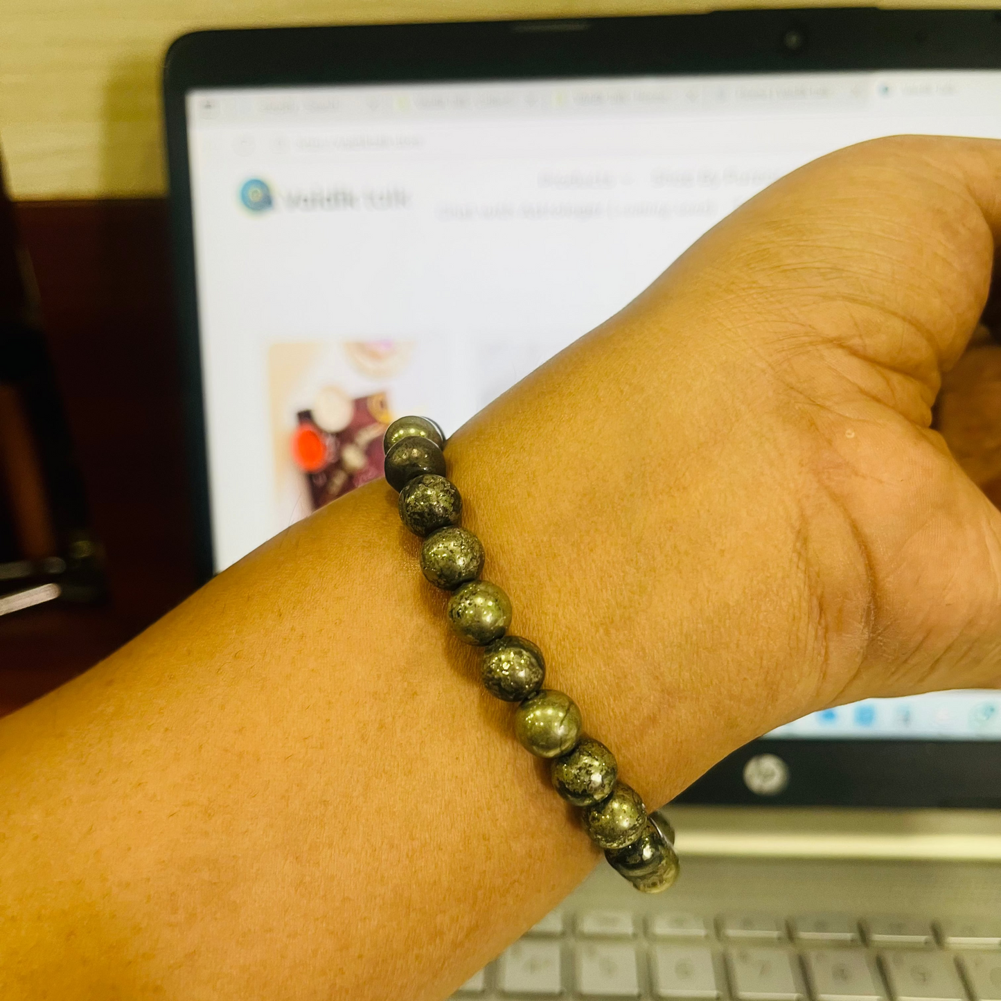 Hand wearing a beaded bracelet in front of a laptop screen