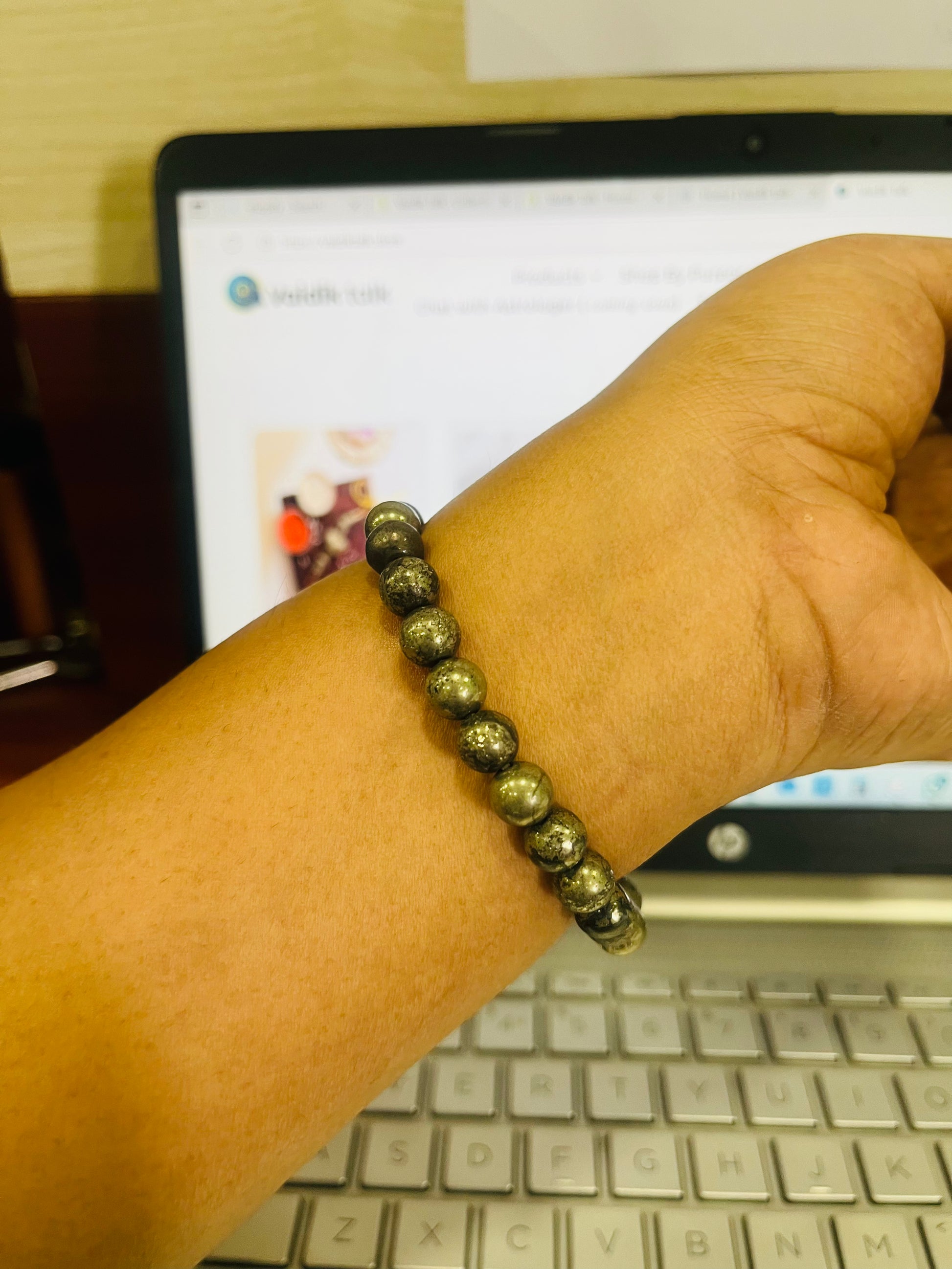 Hand wearing a beaded bracelet in front of a laptop screen